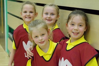 4 young girls in yellow polo shirts with red WDL bibs on in a gym